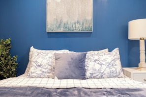 Ein Bett mit einer weiß-blauen Bettdecke, zwei Kissen mit einem Blumenmuster und ein Wandbild darüber.
