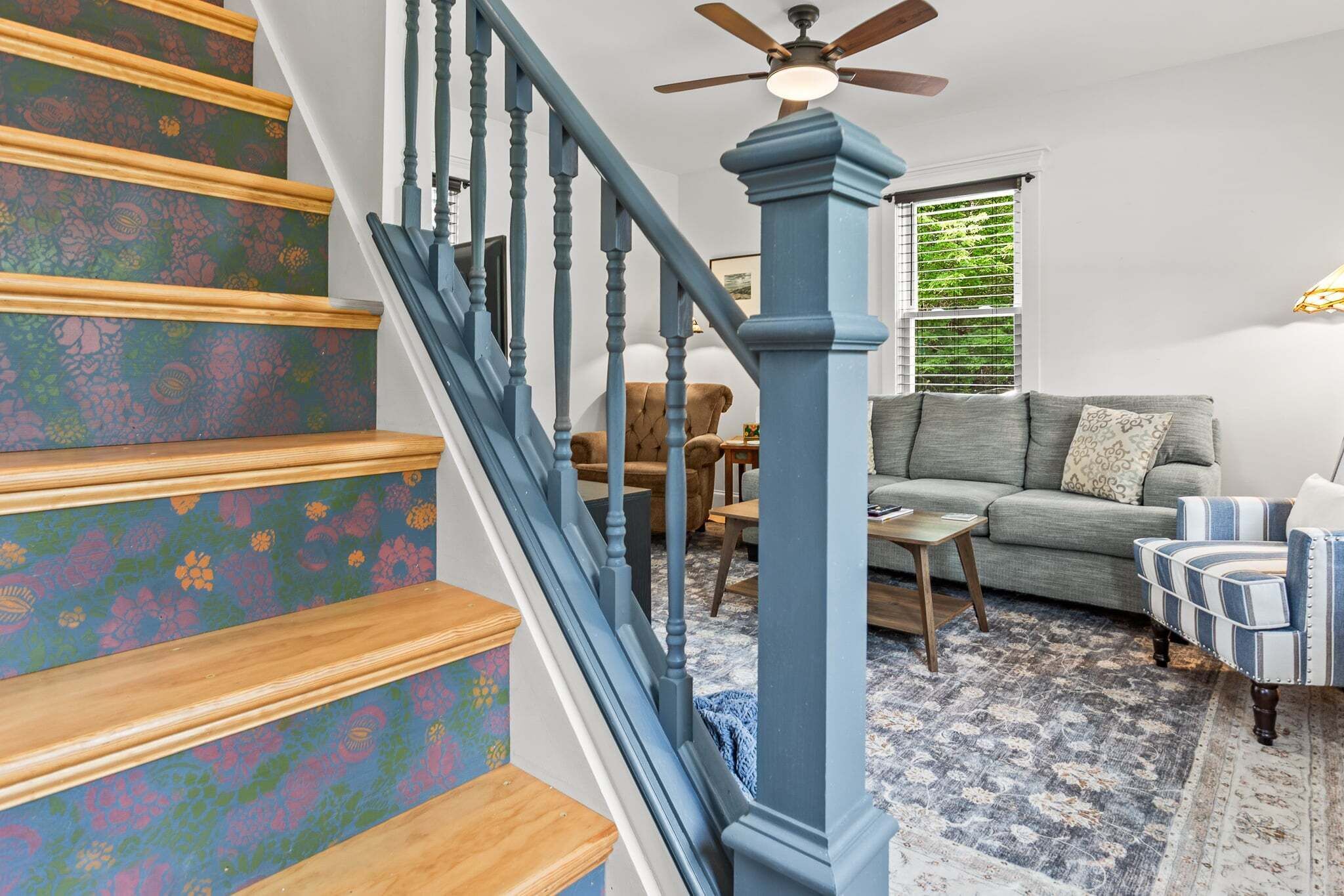 A staircase with wooden steps and blue railings, leading to a living room with a sofa, armchairs, and a coffee table.