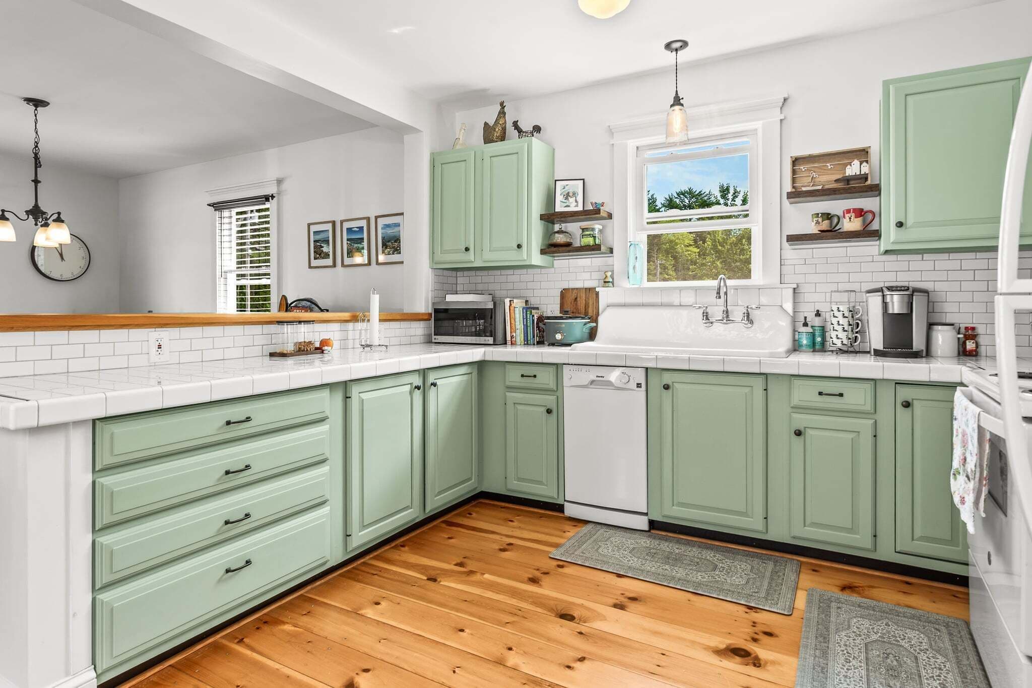 A kitchen with green cabinets, a wooden floor, a window with a view, and various kitchen appliances.
