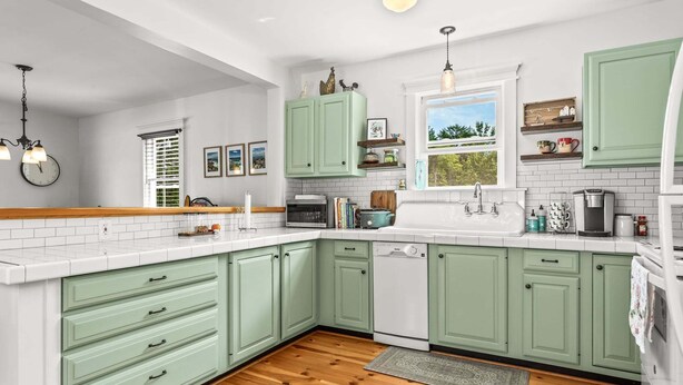 A kitchen with green cabinets, a wooden floor, a window with a view, and various kitchen appliances. - Cross Road Cottage - NEW! Home in Hancock (Hancock)