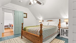 A bedroom with a wooden bed, a ceiling fan, a nightstand with a lamp, and a door leading to another room. - Cross Road Cottage - NEW! Home in Hancock (Hancock)