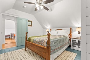 Ein Schlafzimmer mit einem Holzbett, einem Deckenventilator, einem Nachttisch mit Lampe und einer Tür zu einem anderen Raum.