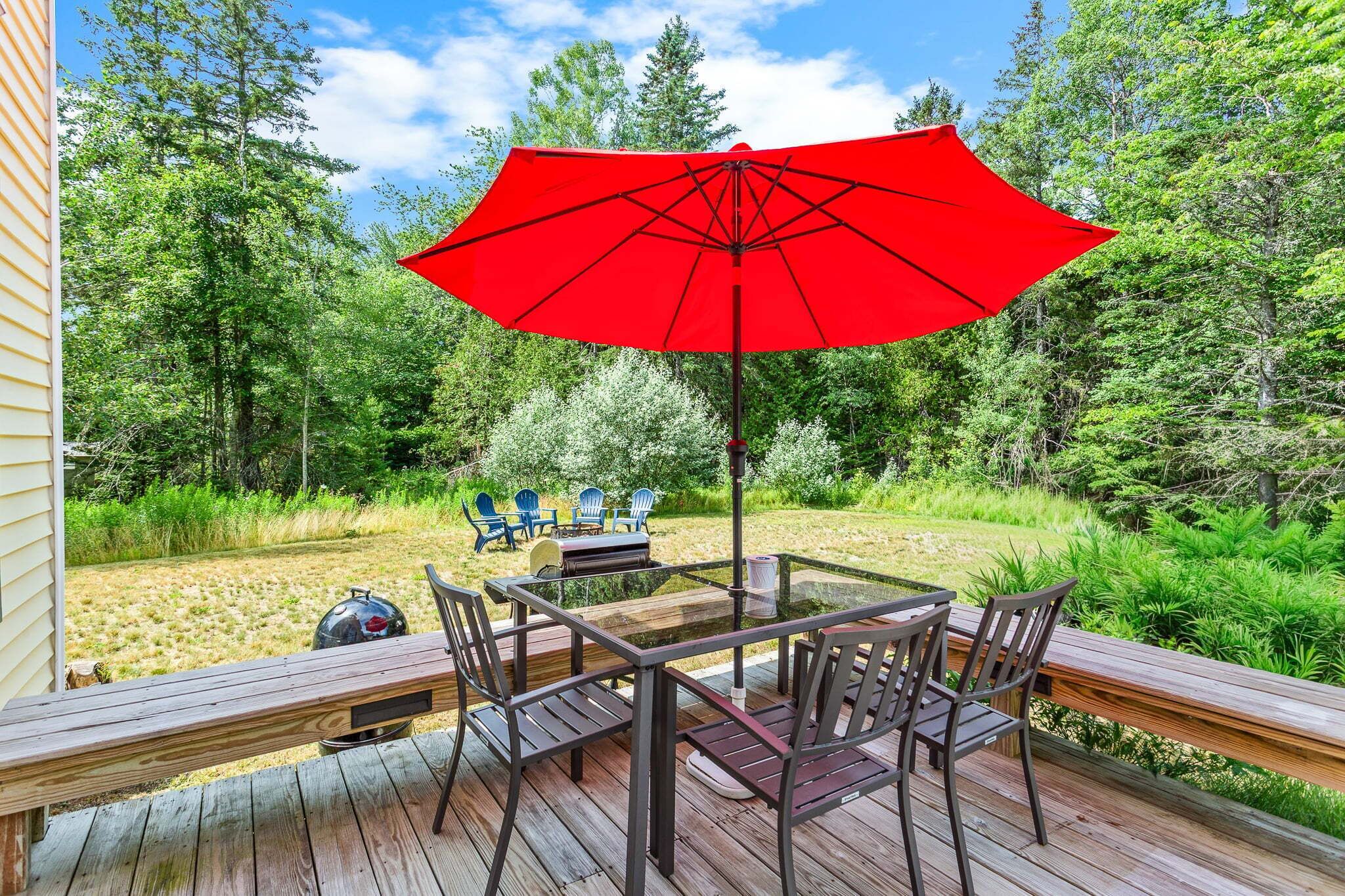 An outdoor deck with a table and chairs, a red umbrella, and a grill.