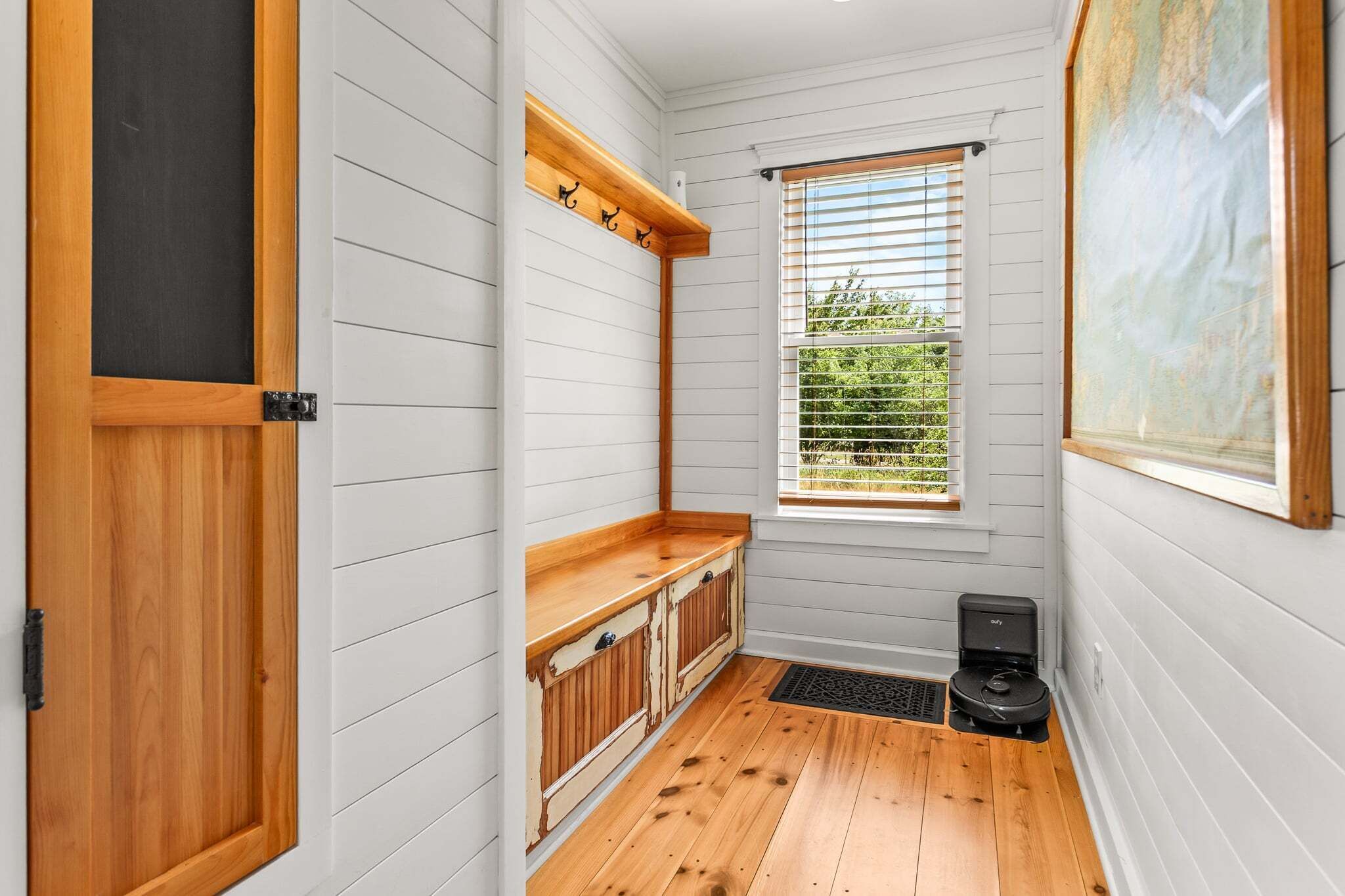 Un pasillo estrecho con suelo de madera, una ventana con persianas, un radiador y una puerta con marco negro.