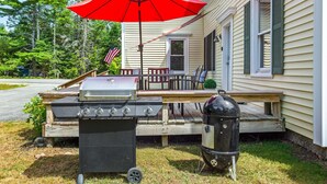A barbecue grill set up on a wooden deck with a red umbrella, a gas grill, and a charcoal grill. - Cross Road Cottage - NEW! Home in Hancock (Hancock)