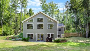 A two-story house with a symmetrical facade, multiple windows, and a covered outdoor grill. - Patten Pond Retreat - NEW! Waterfront (Surry)