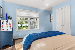 Une chambre à coucher avec un lit, une commode, une fenêtre avec des stores et une porte.