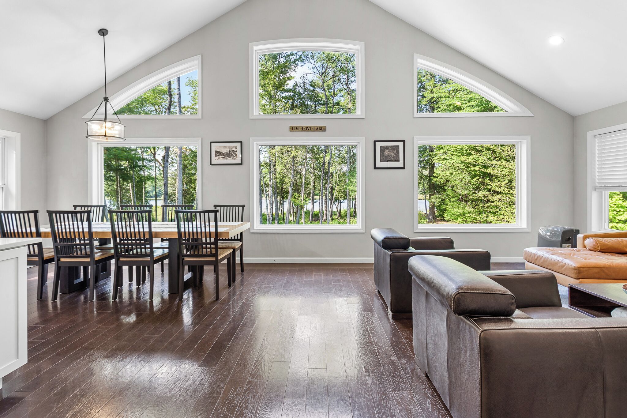 A spacious room with a dining area, a seating area with a sofa, and large windows offering views of trees and a lake.