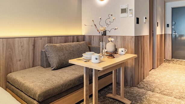 A modern hotel room with a sofa, a small table with a vase and cups, and a wall-mounted light fixture. - Apartment Hotel 11 Namba 2 (Osaka-shi)