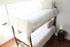 Ein Stockbett mit weißer Bettwäsche, einer Nachttischlampe und Holzboden.