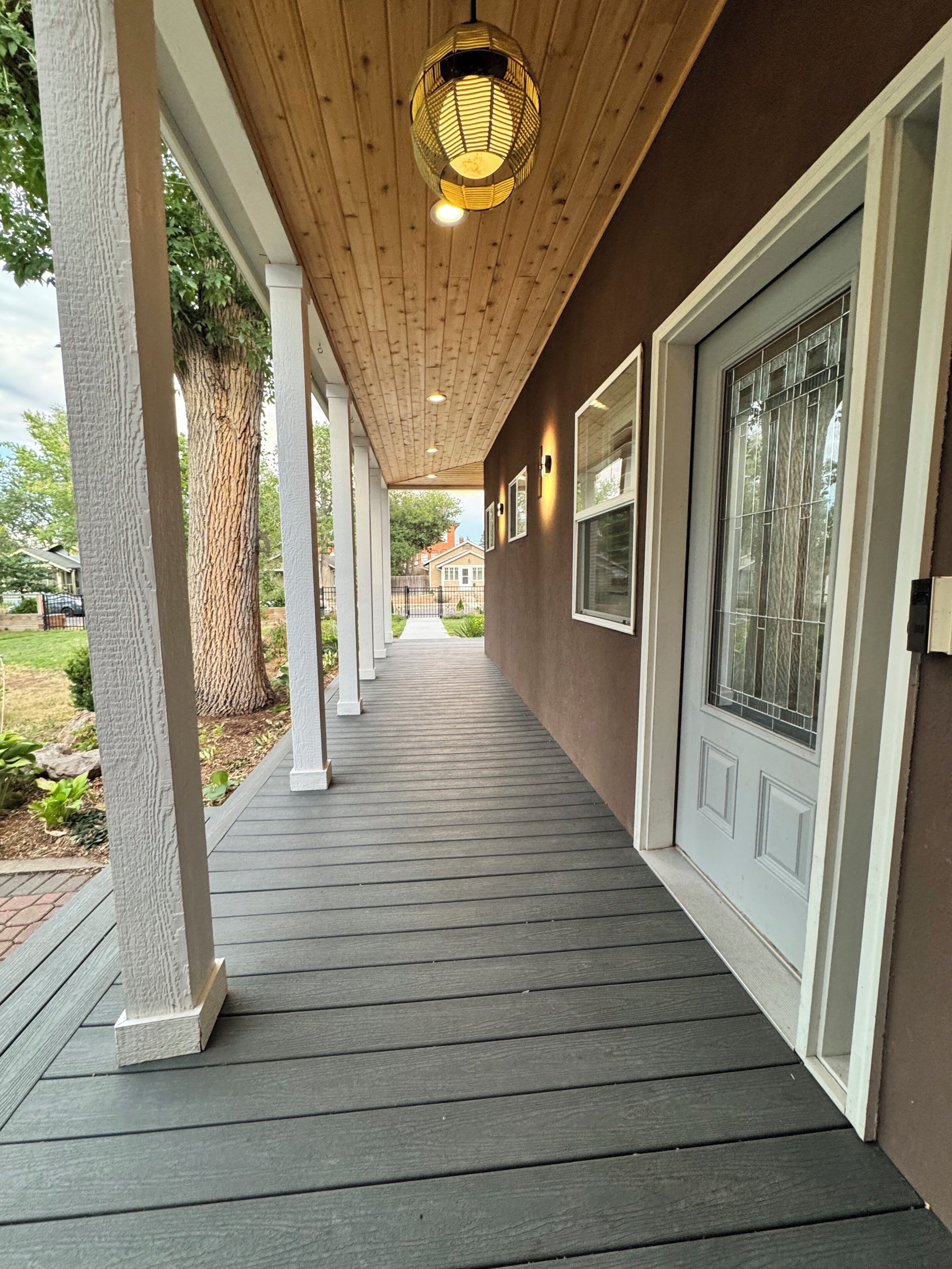 A covered porch with a wooden ceiling, white columns, and a view of the backyard.