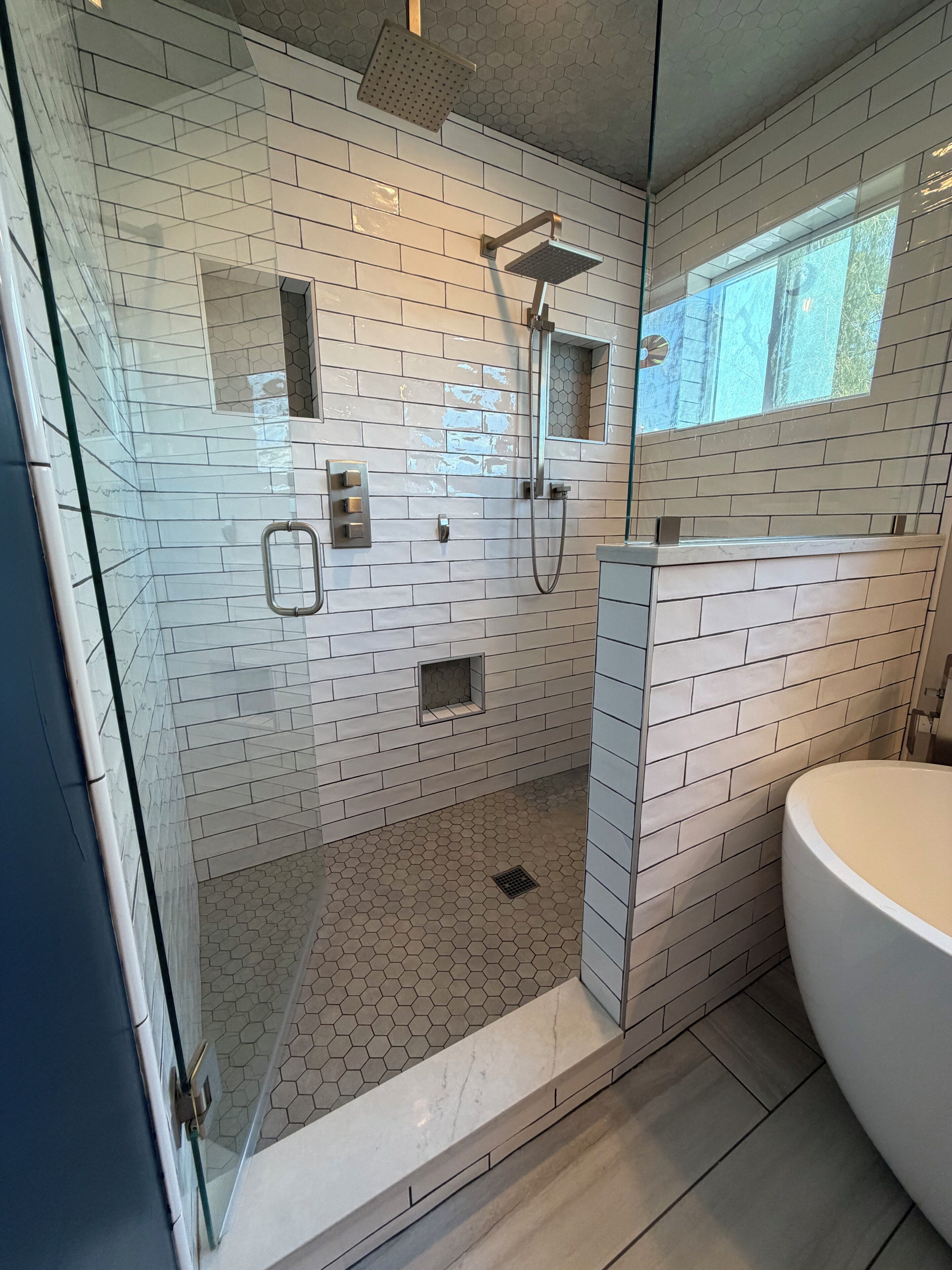 Ett modernt badrum med en dusch som är avskärmad med glasväggar, en vit tvättställ och ett kaklat golv.