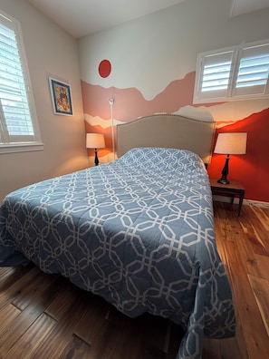 A bedroom with a bed, two bedside lamps, a wall with a red circle, and a window with blinds. - 3-bedroom, 2-bath single-family home with yard and parking (Denver)