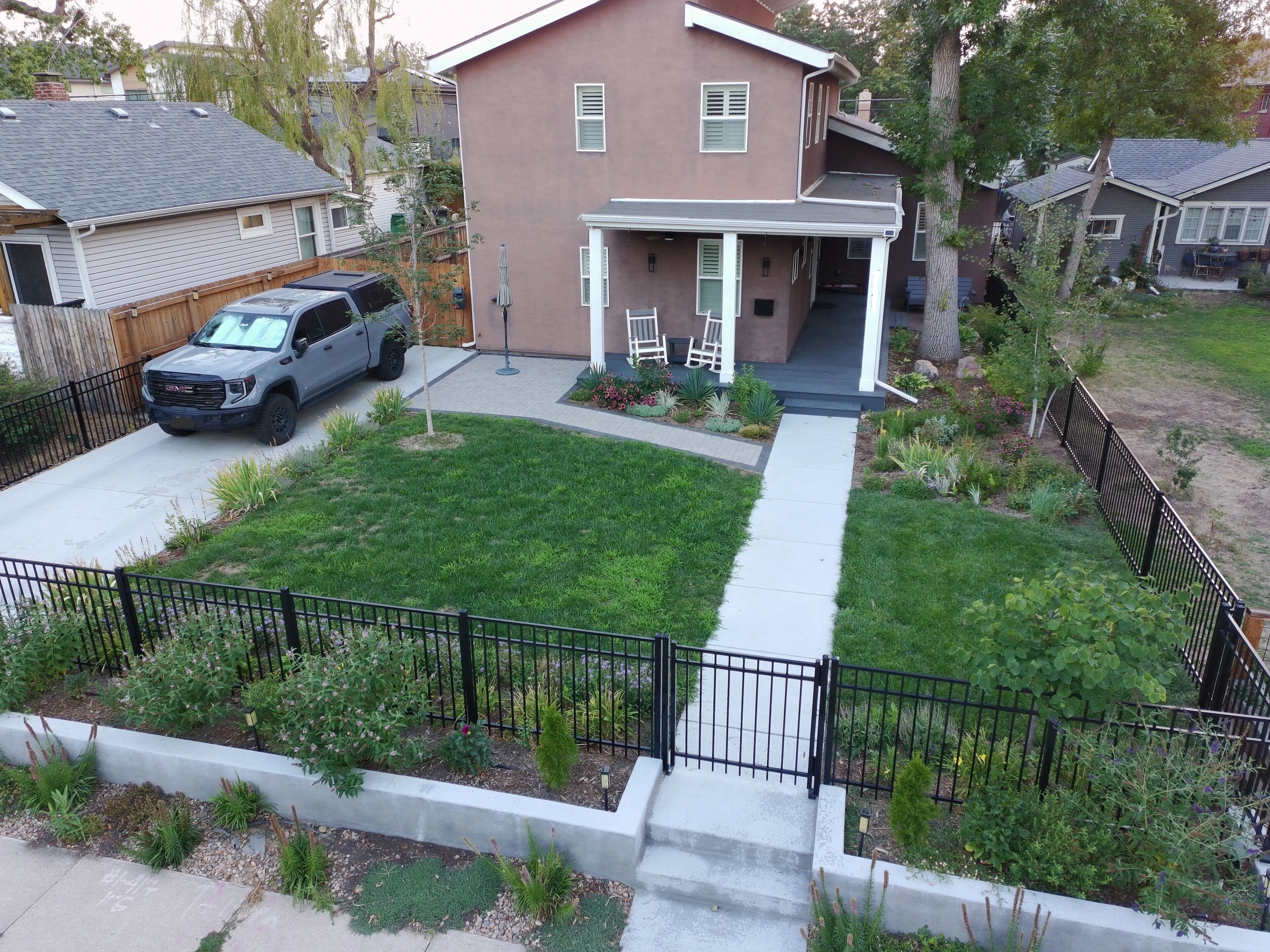 A residential property with a paved driveway, a lawn, and a black metal fence.