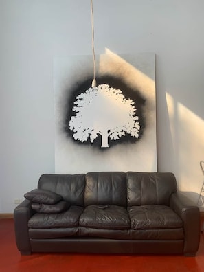 A room with a brown leather sofa and a large abstract tree artwork on the wall.