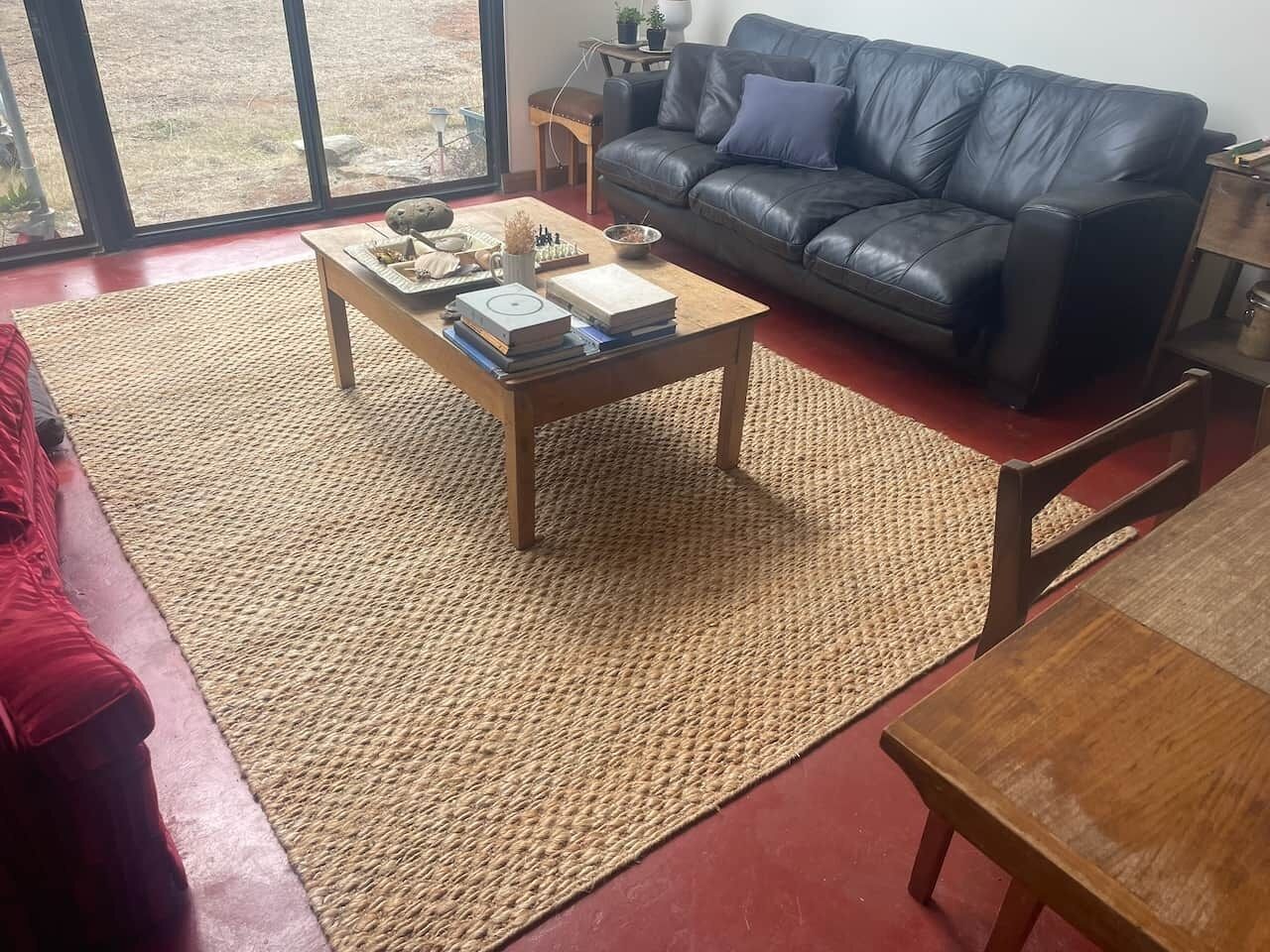 Uma sala de estar com um sofá de couro, uma mesa de centro com livros, um tapete e uma vista através de grandes janelas.
