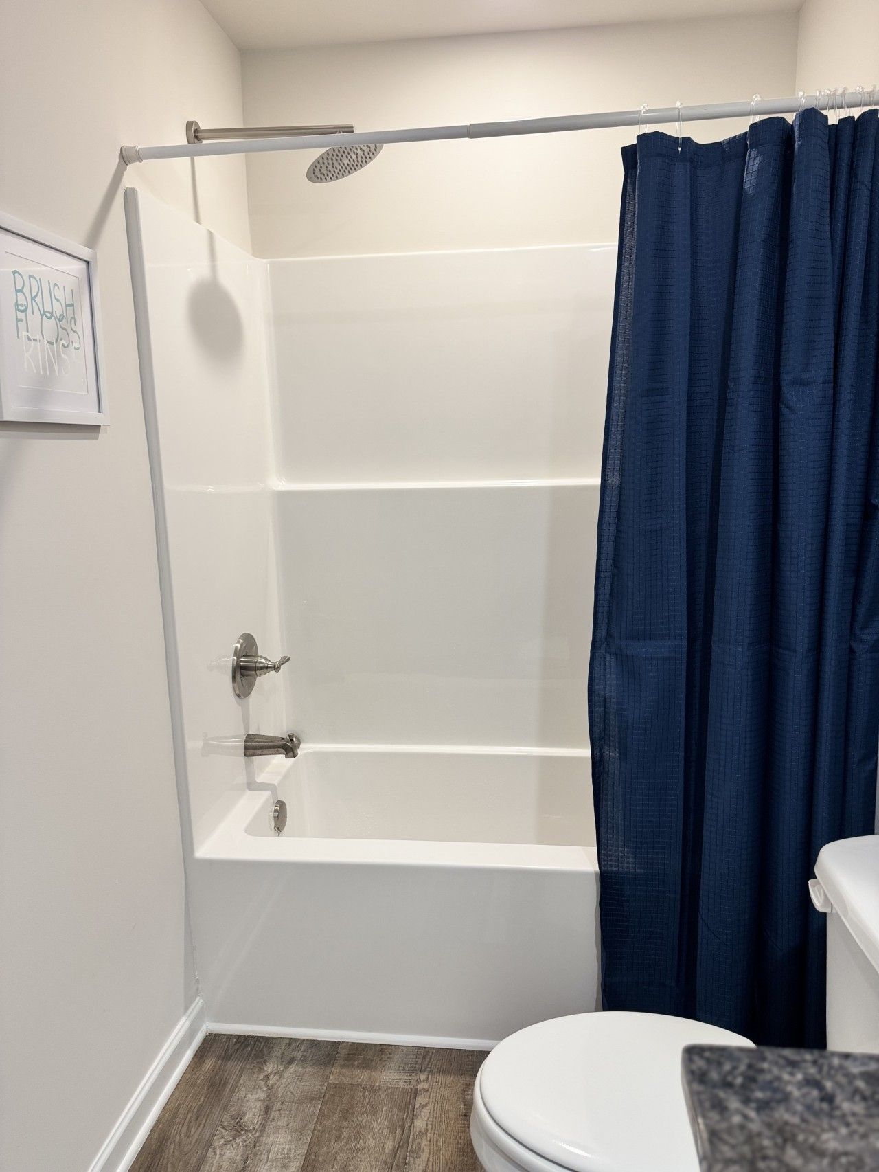 A bathroom with a white bathtub, a shower curtain, a toilet, and a wooden floor.
