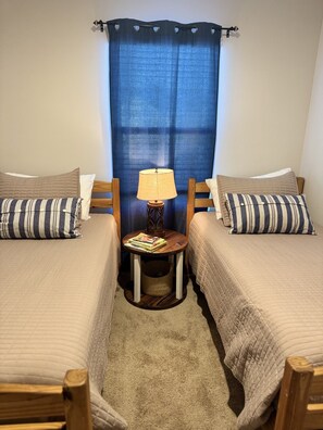 A bedroom with two single beds, a small table with a lamp, and a curtain.