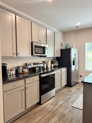 A modern kitchen with light-colored cabinets, stainless steel appliances, and a wooden floor.