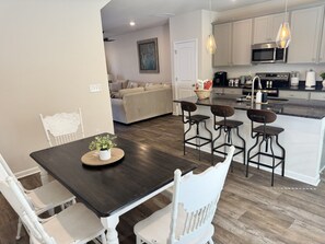 A modern kitchen with a dining area, featuring a dark wood table, white chairs, and a central island with bar stools.