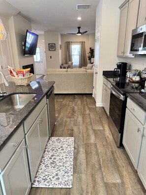 A compact kitchen with a microwave, stove, and sink. A flat-screen TV is mounted on the wall.