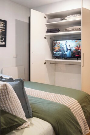 A bedroom with a bed, a TV mounted on a wall, and a shelf above the bed. - Spacious Vibey Retreat with a Movie Projector, Electric Recliner and & Balcony (Melbourne)