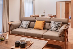 A modern living room with a beige sofa, patterned cushions, a wooden coffee table with mugs, and a dining area in the background. - Apartment Hotel 11 Villa Tengachaya (Osaka-shi)