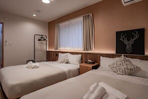 A hotel room with two beds, a bedside table with a lamp, a wall-mounted air conditioner, and a window with curtains. - Apartment Hotel 11 Villa Tengachaya (Osaka-shi)