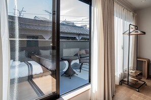 Ett hotellrum med en skjutdörr i glas som leder ut till en balkong med ett bord och stolar, en upphängningsanordning för ytterkläder och ett litet träbord.