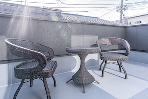 A rooftop terrace with two wicker chairs and a small table, surrounded by a grey wall and a tiled roof.