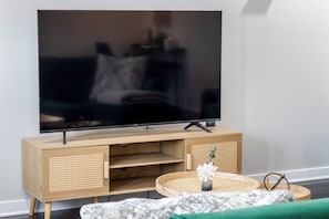 A television on a wooden stand with a woven basket and a small vase on the floor.