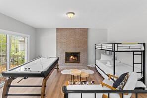 A room with a pool table, a fireplace, bunk beds, and a view of the outdoors.