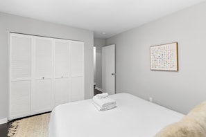 A hotel room with a bed, a white closet, a door leading to another room, and a framed picture on the wall.