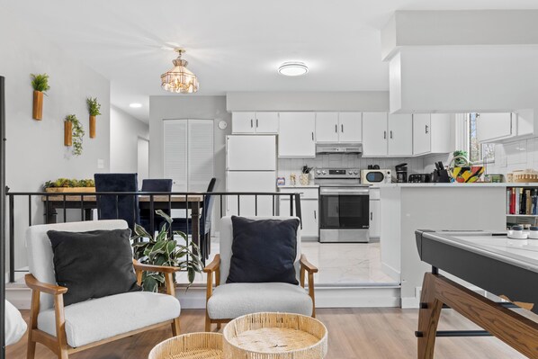 A modern kitchen with white cabinets, a dining area with two chairs, and a hanging light fixture.