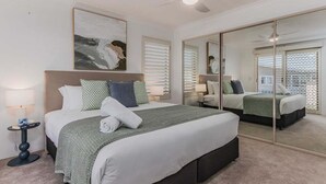 Een slaapkamer met een groot bed, een plafondventilator, een spiegel en een raam met zonwering.