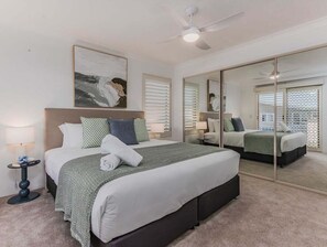 Ein Schlafzimmer mit einem großen Bett, einem Deckenventilator, einem Spiegel und einem Fenster mit Jalousien.