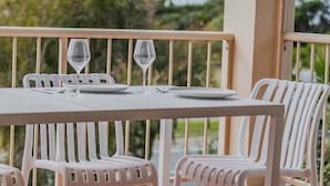 Een witte tafel met twee wijnglazen en borden, omringd door witte stoelen op een balkon met een reling.