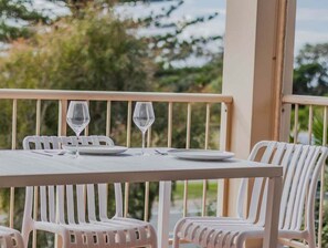 Ein weißer Tisch mit zwei Weingläsern und Tellern, umgeben von weißen Stühlen auf einem Balkon mit Geländer.