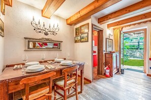 A dining area with a wooden table set for four, a mirror above the table, and a fire extinguisher near the door. - Courmayeur Apartment X6 Parking, Courmayeur, Italy (Courmayeur)