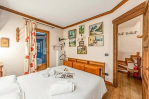 A hotel room with a bed, a wooden headboard, a window with a curtain, a radiator, a wall-mounted shelf, and a staircase. - Courmayeur Apartment X6 Parking, Courmayeur, Italy (Courmayeur)