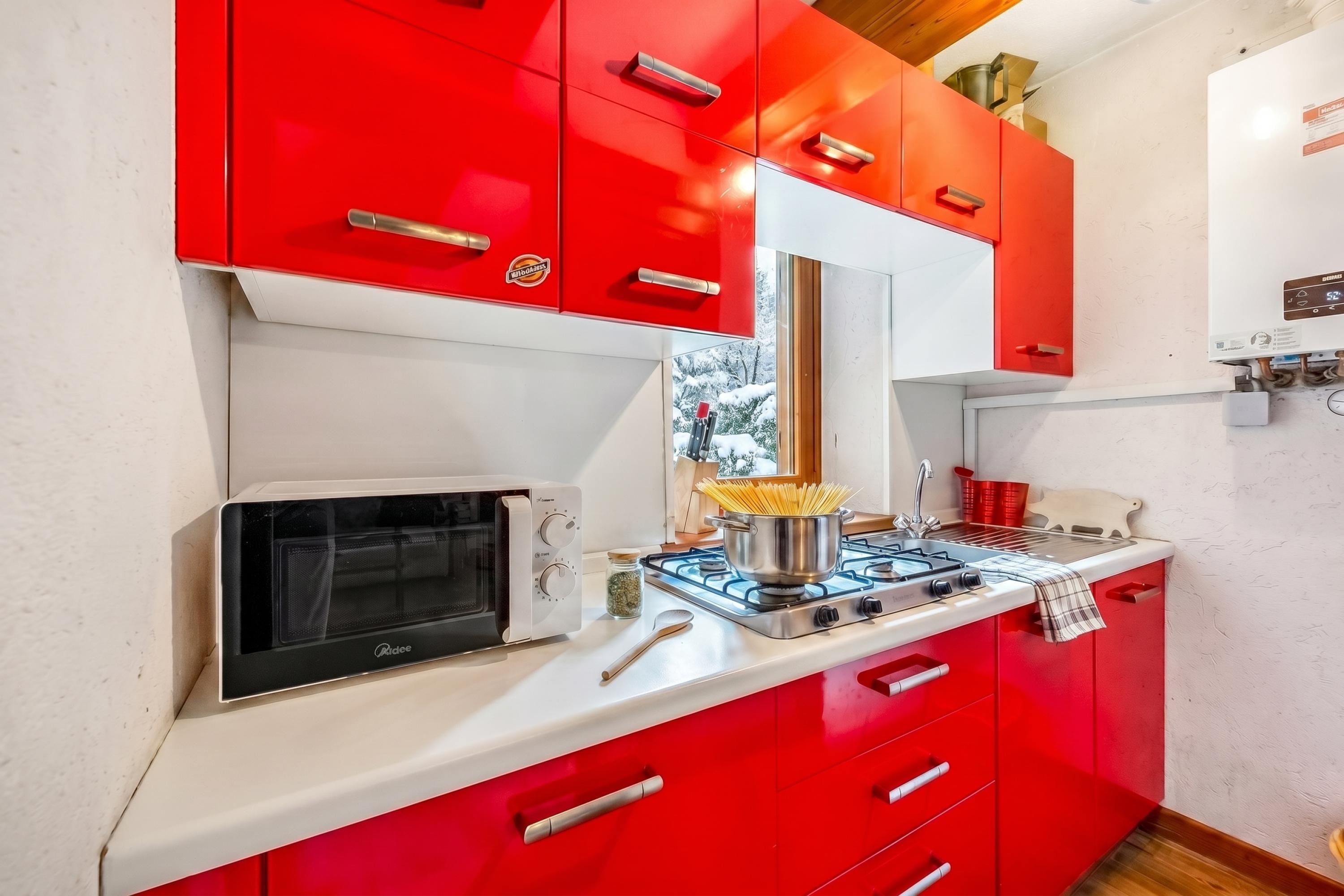 A kitchen with red cabinets, a microwave, a gas stove, and a window with a snowy view.