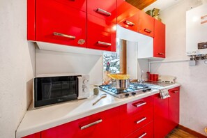 Cozinha com armários vermelhos, micro-ondas, fogão a gás e janela com vista para neve.