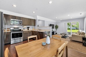 A modern kitchen with stainless steel appliances, wooden cabinets, and a dining area with a wooden table and chairs.