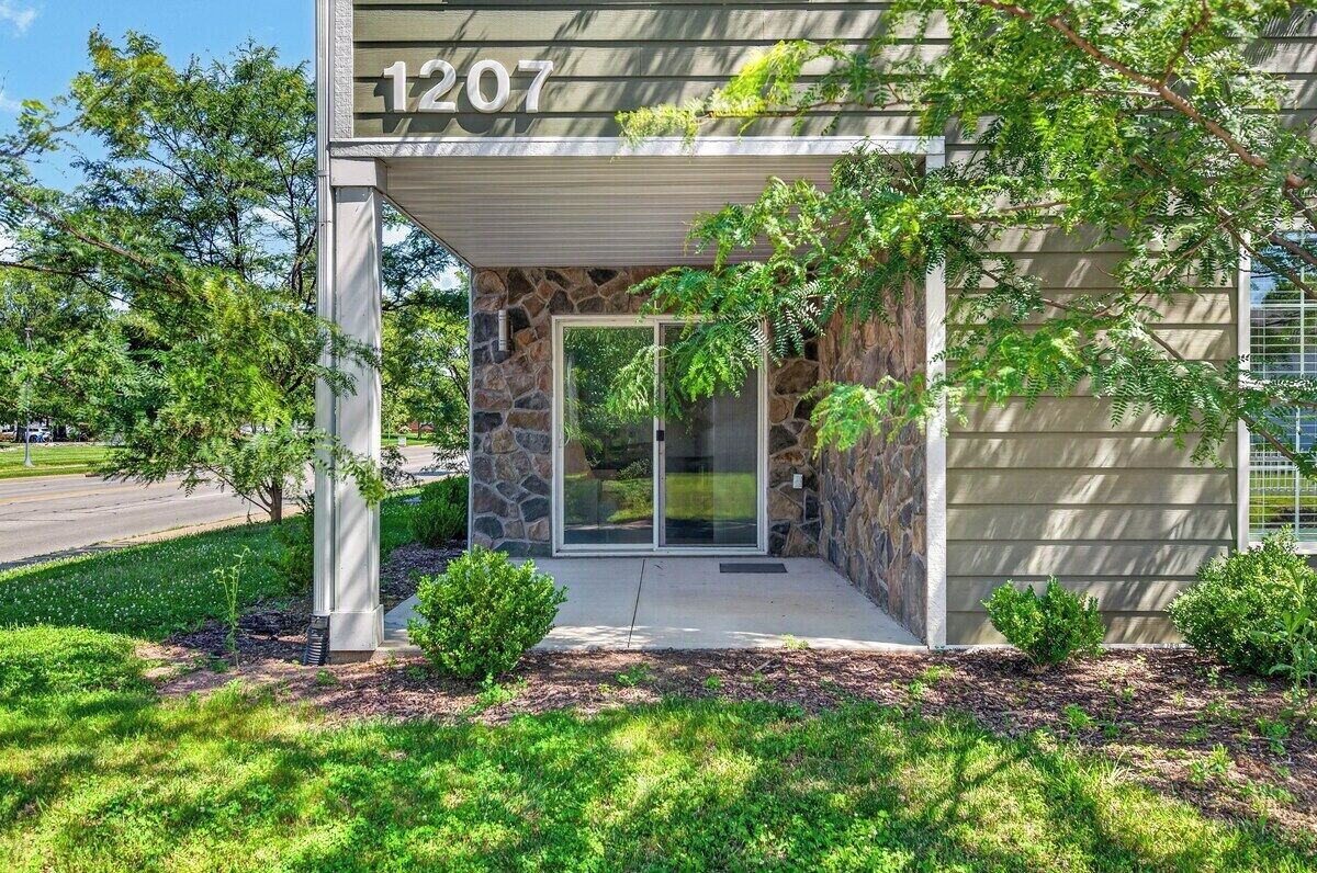 A building with a stone facade, a glass entrance, and a number '1207' above the door.