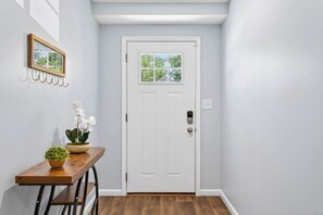 A hallway with a white door, a small table with a potted plant, and a wall-mounted picture frame.