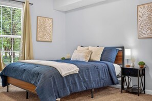 Une chambre à coucher avec un lit, une table de chevet et une fenêtre avec des rideaux.