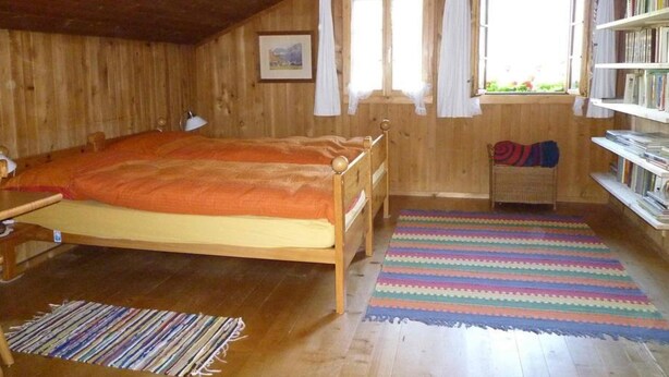 A wooden room with a bed, a desk, a bookshelf, and a window with curtains. - Auf der Mauer Appartement/Fewo, Dusche oder Bad, WC, 2 Schlafräume by Interhome (Oberwil)