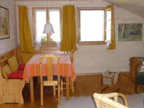Uma área de jantar acolhedora com uma mesa posta para quatro pessoas, cadeiras de madeira, um banco com almofadas e um candeeiro pendente.
