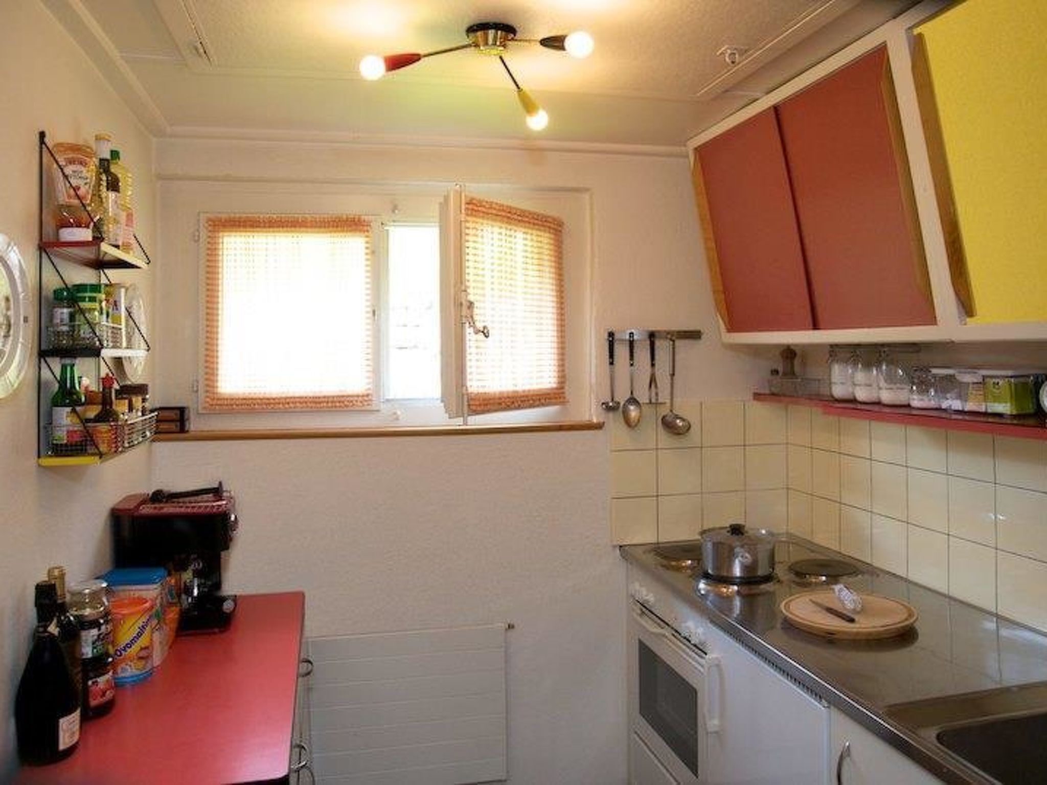A kitchen with a red countertop, a stove, and a window with blinds.