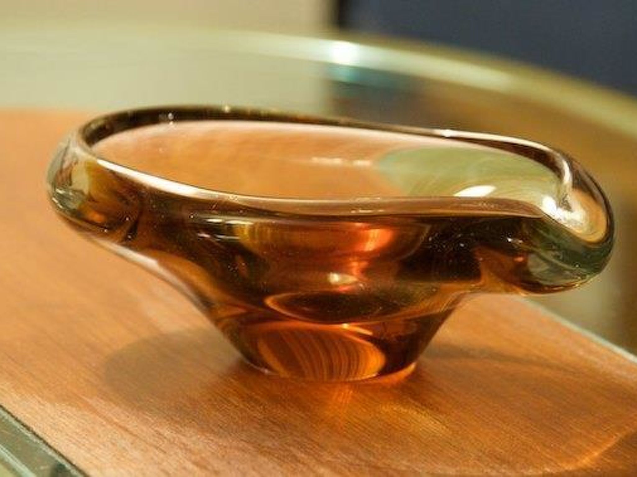 Un objeto de vidrio transparente con superficie reflectante, posiblemente decorativo, sobre una superficie de madera.